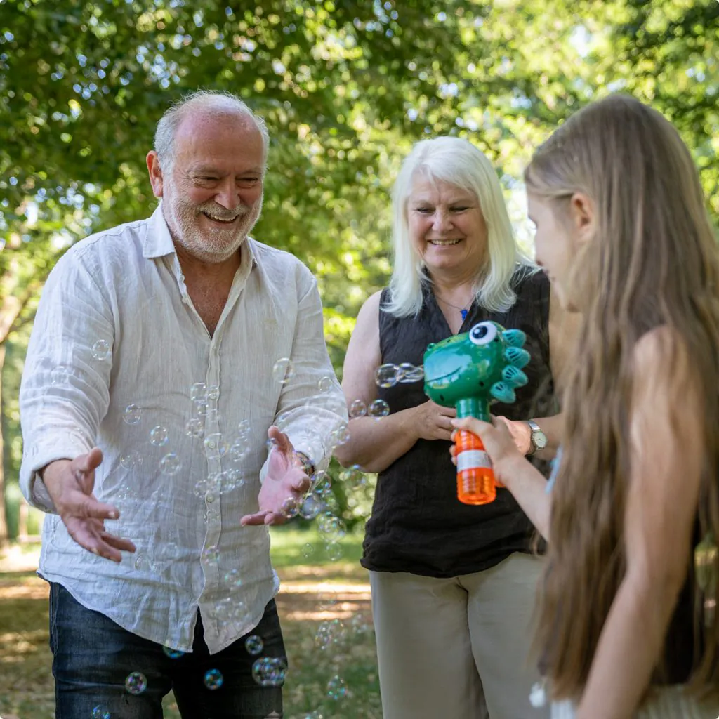 Großeltern und Enkelin lassen gemeinsam Seifenblasen steigen und teilen einen fröhlichen Moment im Park.