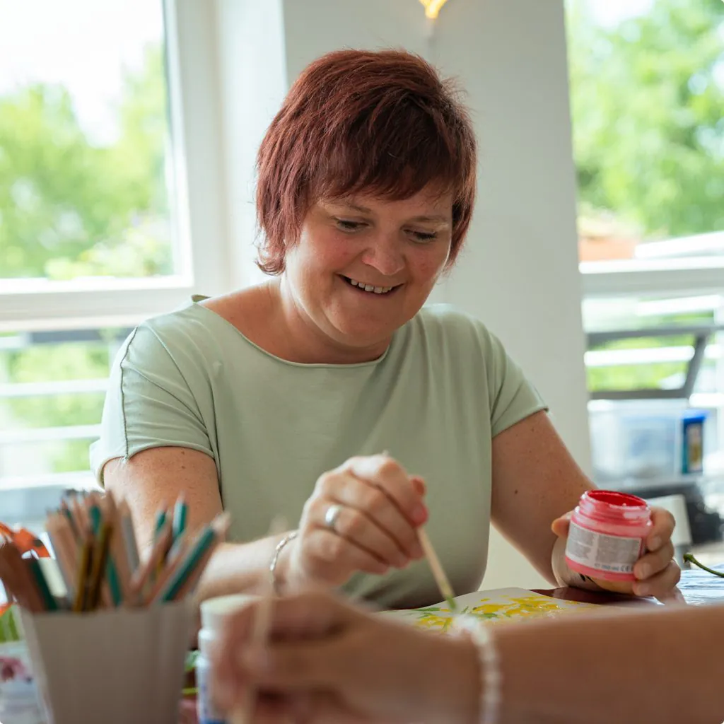 Frau malt konzentriert und mit sichtlicher Freude an einem kleinen Kunstwerk.