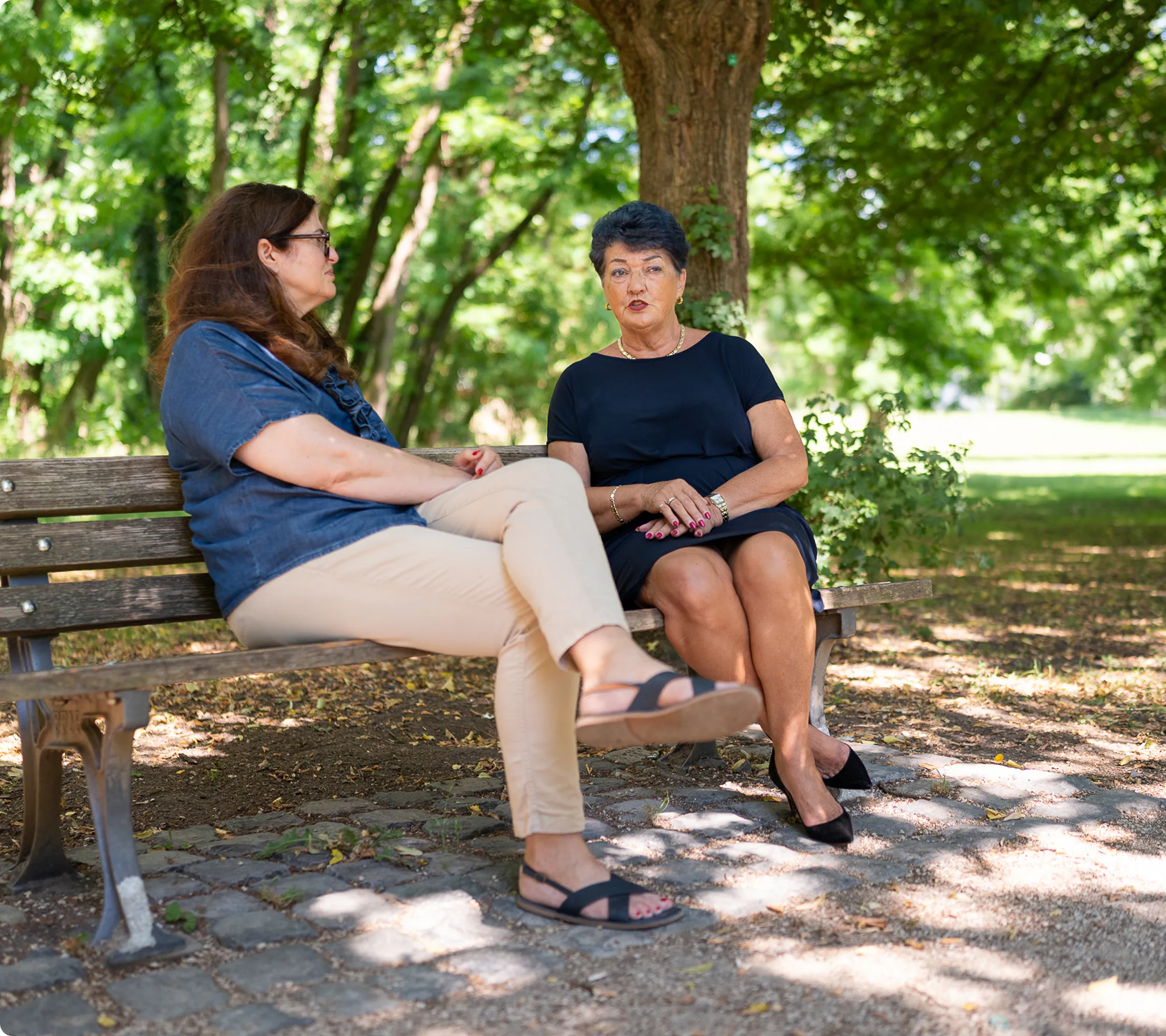Zwei Frauen sitzen im Park auf einer Bank und führen ein vertrautes Gespräch.